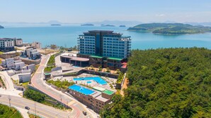 A modern hotel with a central building, swimming pools, and a view of a lake and mountains. - Hotel JCS Yeosu (Yeosu)
