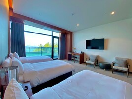 A hotel room with two beds, a desk, a chair, a TV, and a balcony with a view.