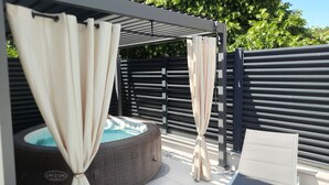 Un espace bien-être comprenant un jacuzzi, une pergola avec des rideaux et un coin salon.