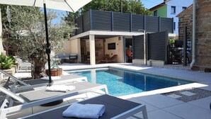 Un espace piscine extérieur moderne, doté de chaises longues et d’un coin salon abrité.
