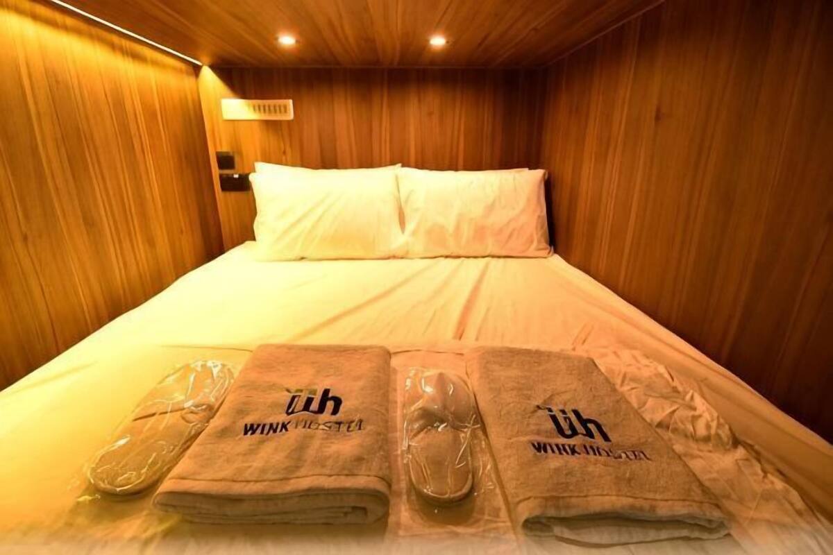 Quarto de hotel com paredes de madeira, cama com roupa de cama branca e toalhas com o nome do hotel.