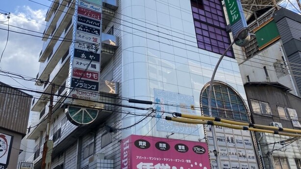 A multi-story building with various commercial signs, including a prominent red sign for 'Navi' and a green sign for 'Coin-Laundry'. - Chintai Navi Hostel (Osaka)