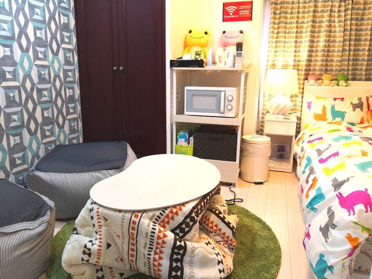 Mukava hotellihuone, jossa on sänky, pyöreä pöytä, mikroaaltouuni ja pieni hylly, jonka päällä on pehmoleluja.