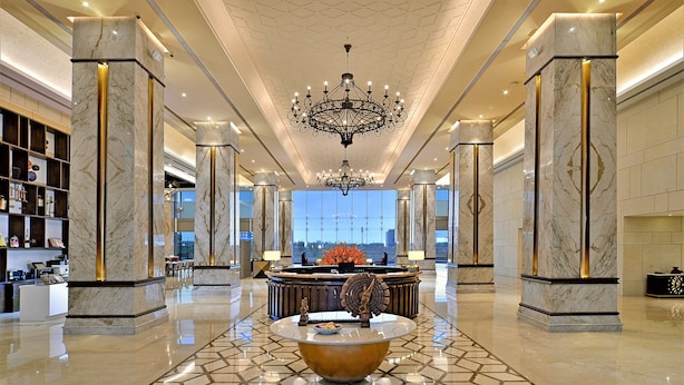 A spacious lobby with marble columns, a central chandelier, and a reception desk. - Gift City Club – a member of Radisson Individuals (Gandhinagar)