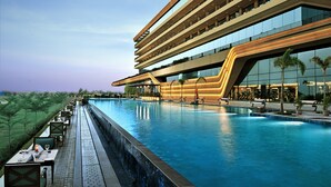 A modern hotel with a large pool, outdoor seating, and a unique architectural design. - Gift City Club – a member of Radisson Individuals (Gandhinagar)