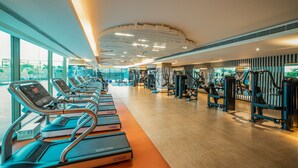 A modern gym with treadmills, weight machines, and a large window offering a view of the city. - Gift City Club – a member of Radisson Individuals (Gandhinagar)