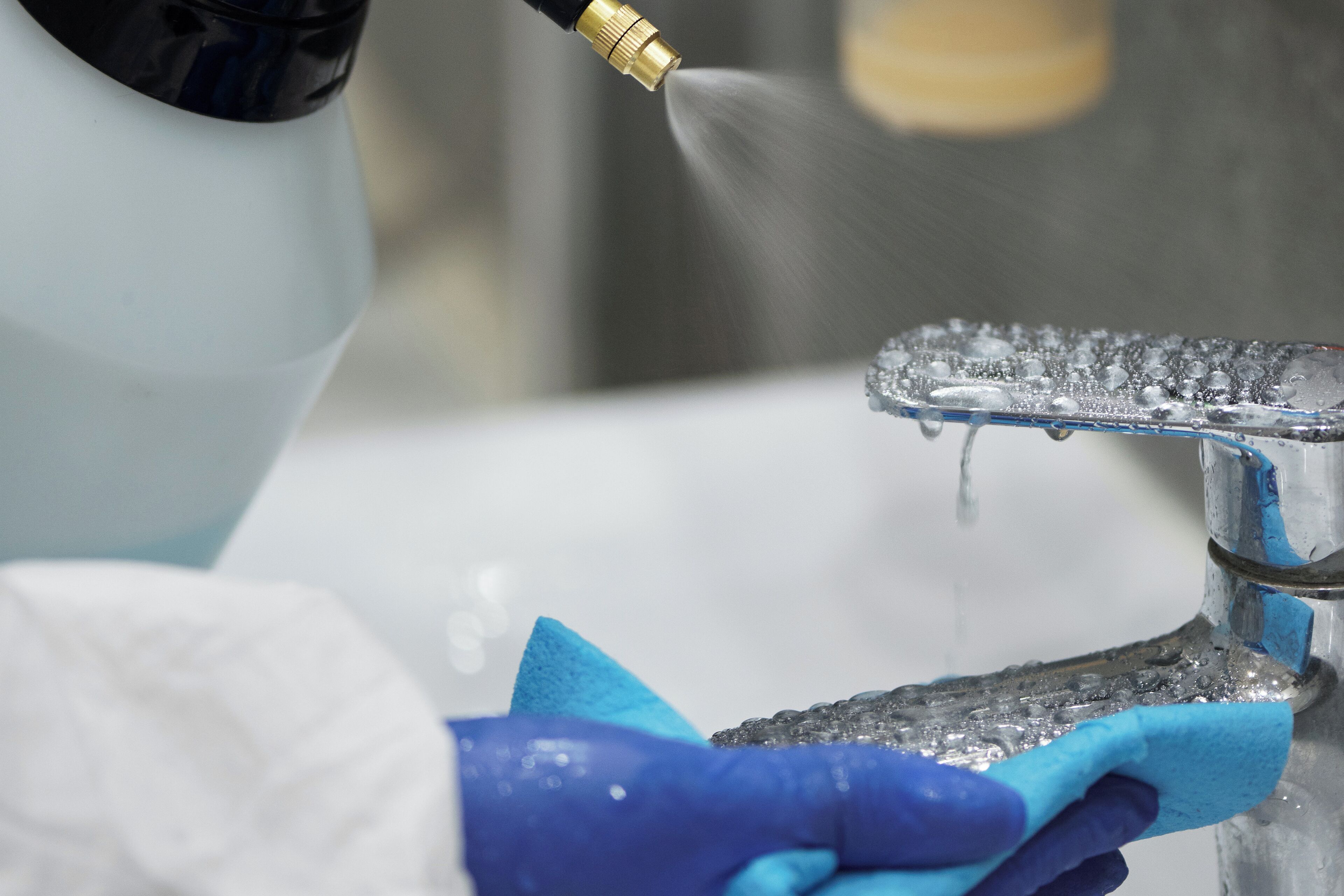 A person wearing gloves cleaning a faucet with a spray bottle.
