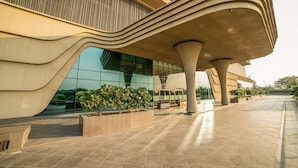 A modern building with unique wavy architectural design, large glass windows, and a spacious outdoor area with planters. - Gift City Club – a member of Radisson Individuals (Gandhinagar)