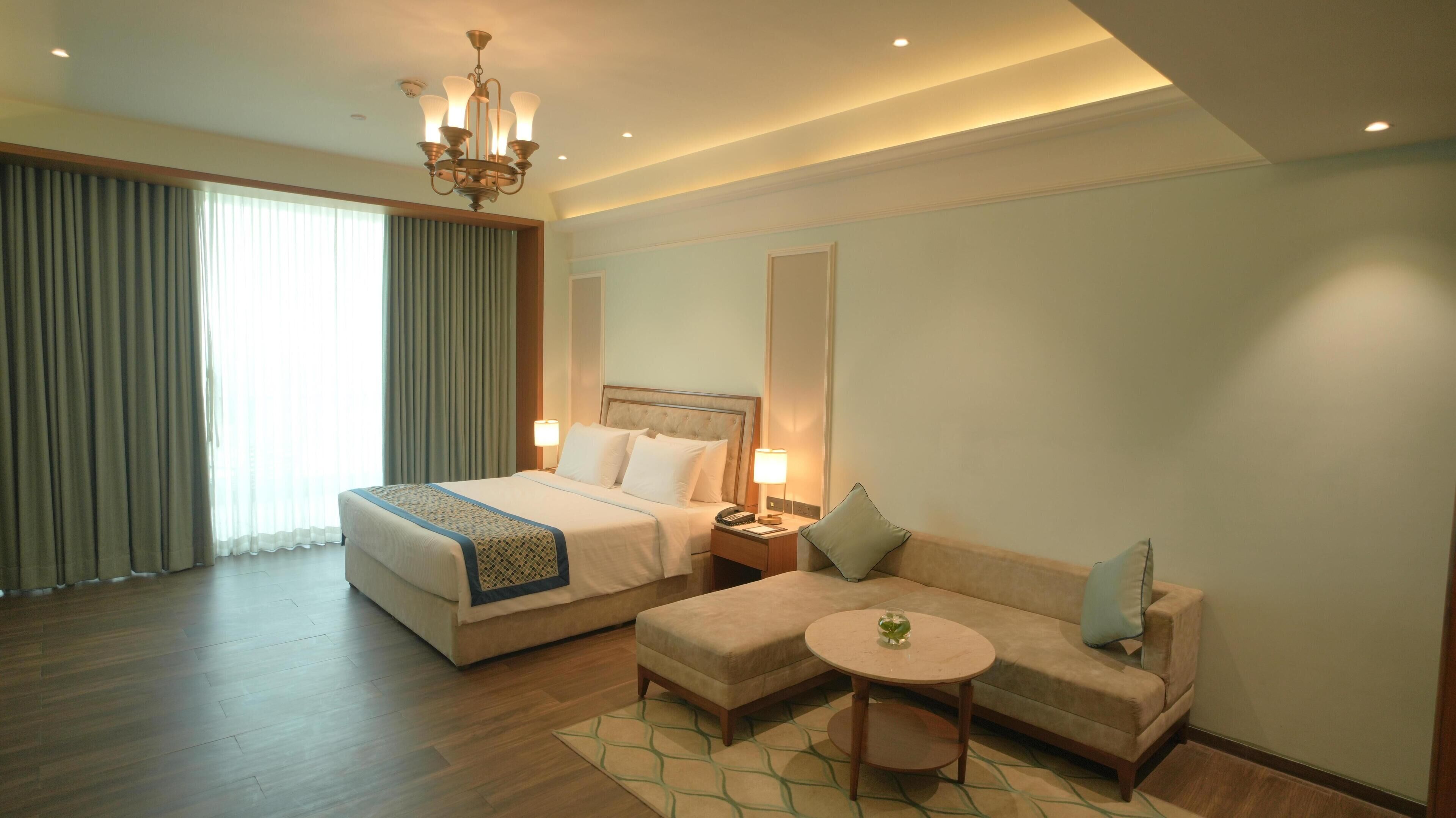 A hotel room with a large bed, a sofa, a small table, and a chandelier.