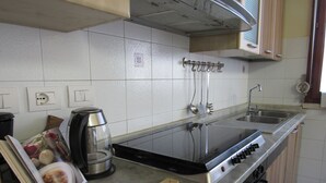 Een keuken met een fornuis, spoelbak en diverse keukengerei.