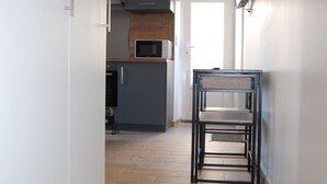 Un pasillo estrecho con una zona de cocina al fondo, una mesa de comedor con sillas y una puerta que da a otra habitación.