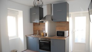 Una cocina compacta con gabinetes grises, una campana extractora de acero inoxidable, un microondas y un horno empotrado.
