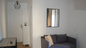 Una sala moderna con un sofá gris, una mesita, una lámpara colgante y un espejo en la pared.