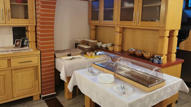 A breakfast buffet setup with wooden cabinets, a brick wall, and a window with blinds. - Rooms and Apartments Panker (Moravske Toplice)