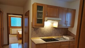 A kitchen with wooden cabinets, a built-in stove, and a window with blinds. - Rooms and Apartments Panker (Moravske Toplice)