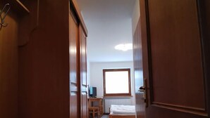 A narrow hallway with wooden doors and a ceiling light. A bed and a desk with a chair are visible in the background. - Rooms and Apartments Panker (Moravske Toplice)