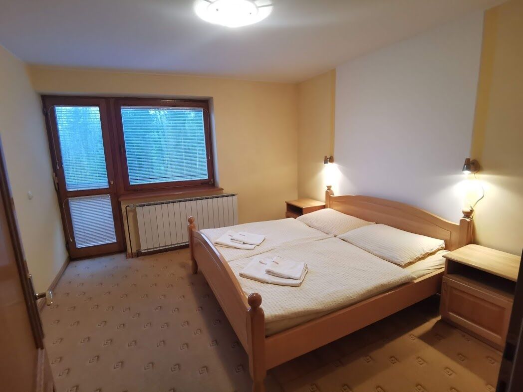 A bedroom with a wooden bed, two bedside lamps, a radiator, and a window with blinds.