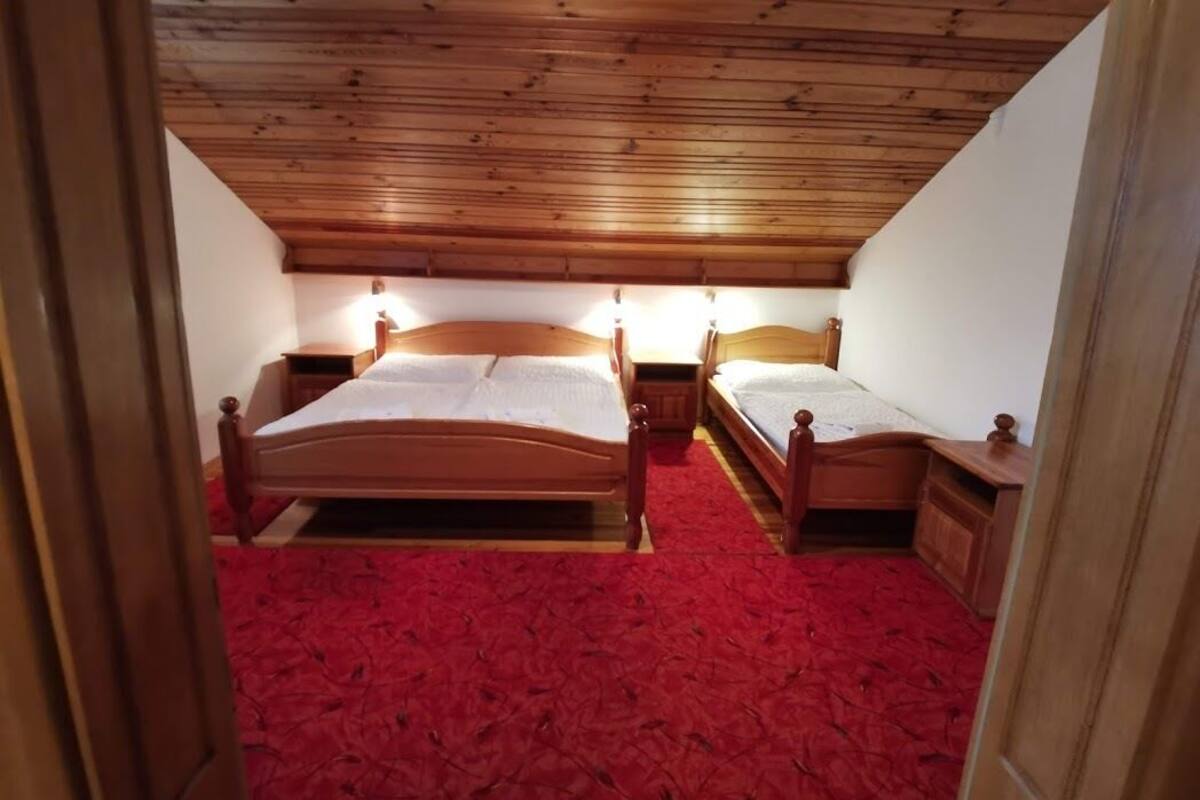 Ein Zimmer mit zwei Holzbett, einem roten Teppich und einer schrägen Decke.