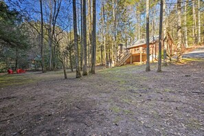 A rustic cabin in a forested area with a dirt ground and a wooden staircase leading to the main entrance. - Blue Ridge Mtns Creekside Cabin w/ Hot Tub + Pier! (Blue Ridge)