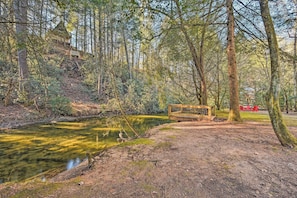 A forested area with a small wooden bridge over a stream, surrounded by trees and a picnic table with chairs. - Blue Ridge Mtns Creekside Cabin w/ Hot Tub + Pier! (Blue Ridge)