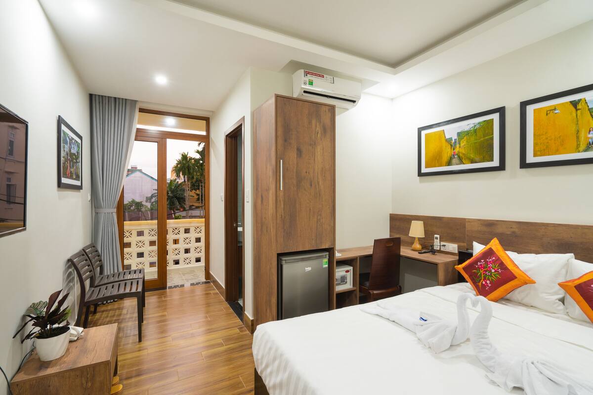 A hotel room with a bed, a desk, a chair, a small refrigerator, and a wardrobe.