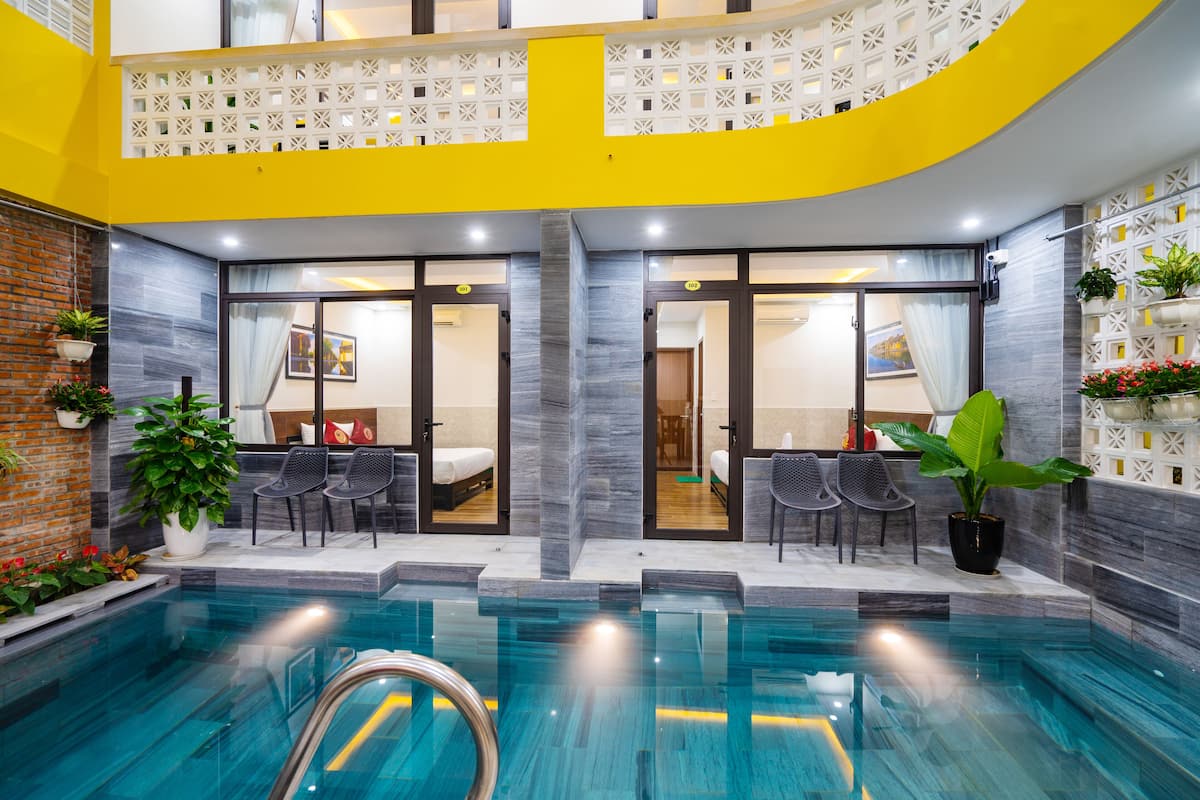 An indoor swimming pool with a modern design, featuring a yellow accent wall, a brick wall on one side, and a seating area with chairs and a table.