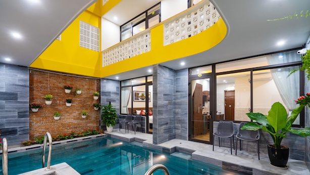 A modern indoor pool area with a brick wall, seating, and potted plants. - The Lit Villa (Da Nang)