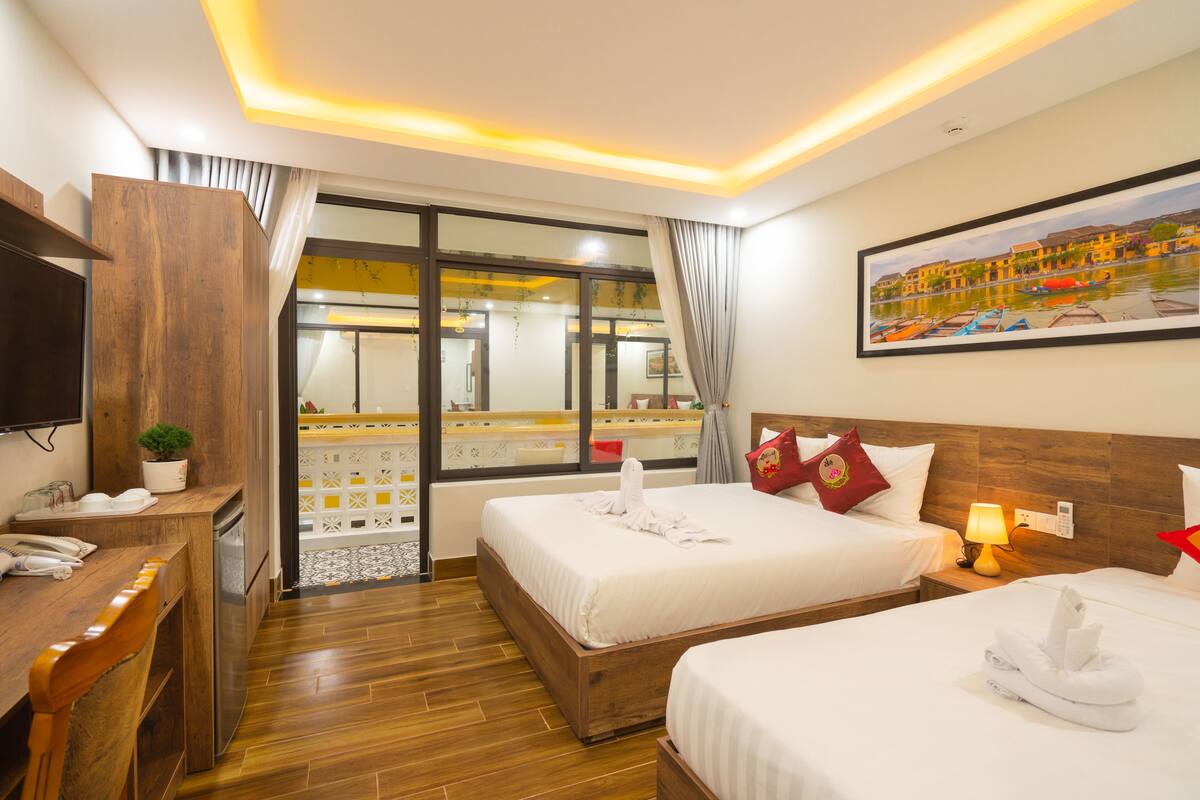 A hotel room with two beds, a desk, a TV, a window with curtains, and a painting on the wall.