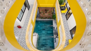 A high-ceiling atrium with a central pool, surrounded by yellow walls and patterned flooring. - The Lit Villa (Da Nang)