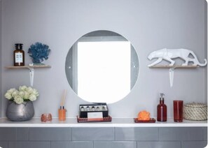 Bathroom features a large round mirror above a white countertop with two shelves and a vase of flowers.