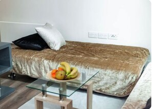 Cozy retreat with a single bed, glass-top table, and a bowl of fresh fruit.