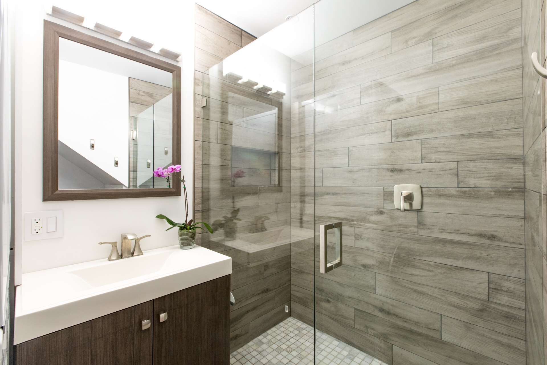 A modern bathroom with a wooden vanity, a mirror, and a shower with a glass door.