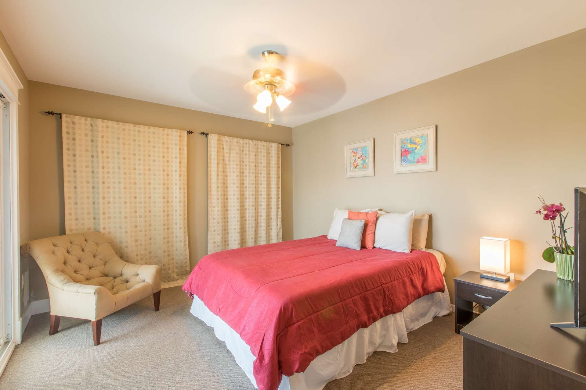 Una habitación de hotel con una cama, una silla, un escritorio y un ventilador de techo.