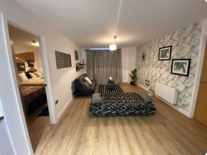 Cozy living space with a sofa, side table, and potted plant, featuring a bed in the background.