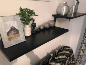 A serene space features a shelf with a framed landscape, a vase, a sculpture, and decorative spheres, complemented by a striped throw.