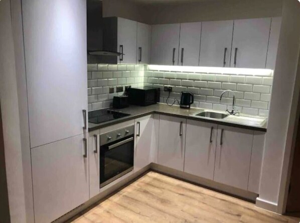 Compact kitchen with oven, stovetop, and sink, featuring light-colored cabinets and a backsplash with white tiles.