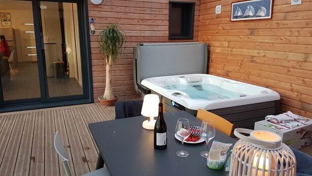Een houten hut met een jacuzzi, een eettafel met wijn en een lantaarn.