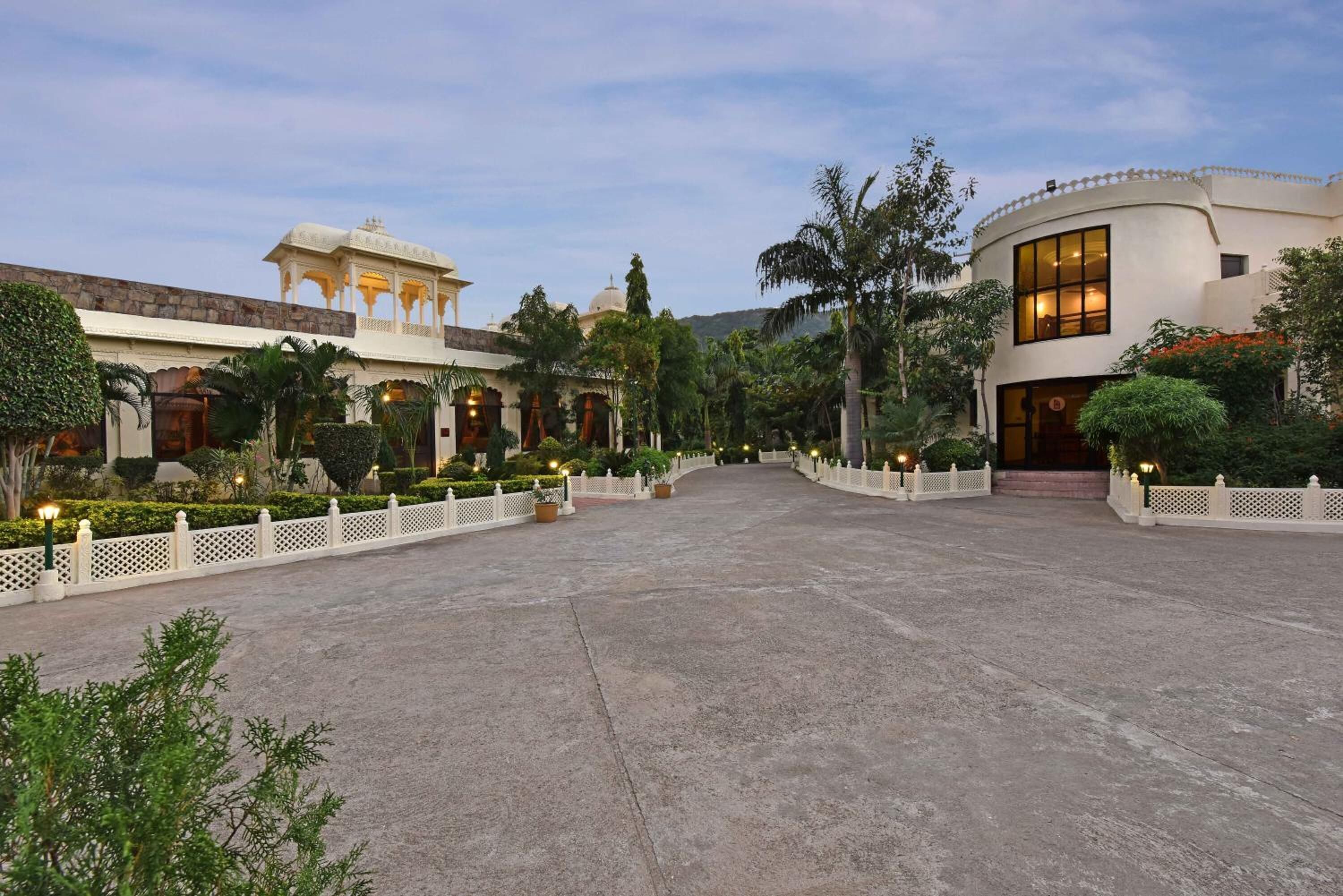 A spacious courtyard with a white fence, palm trees, and a building with a dome and arches.