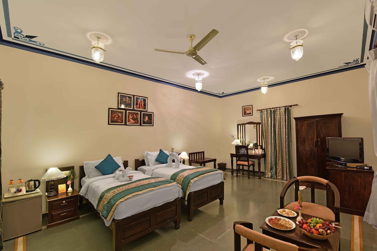 A hotel room with two beds, a desk, a chair, a television, and a ceiling fan.