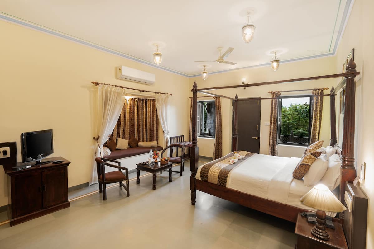 A four-poster bed with a canopy, a television on a cabinet, a desk with a lamp, and a chair.