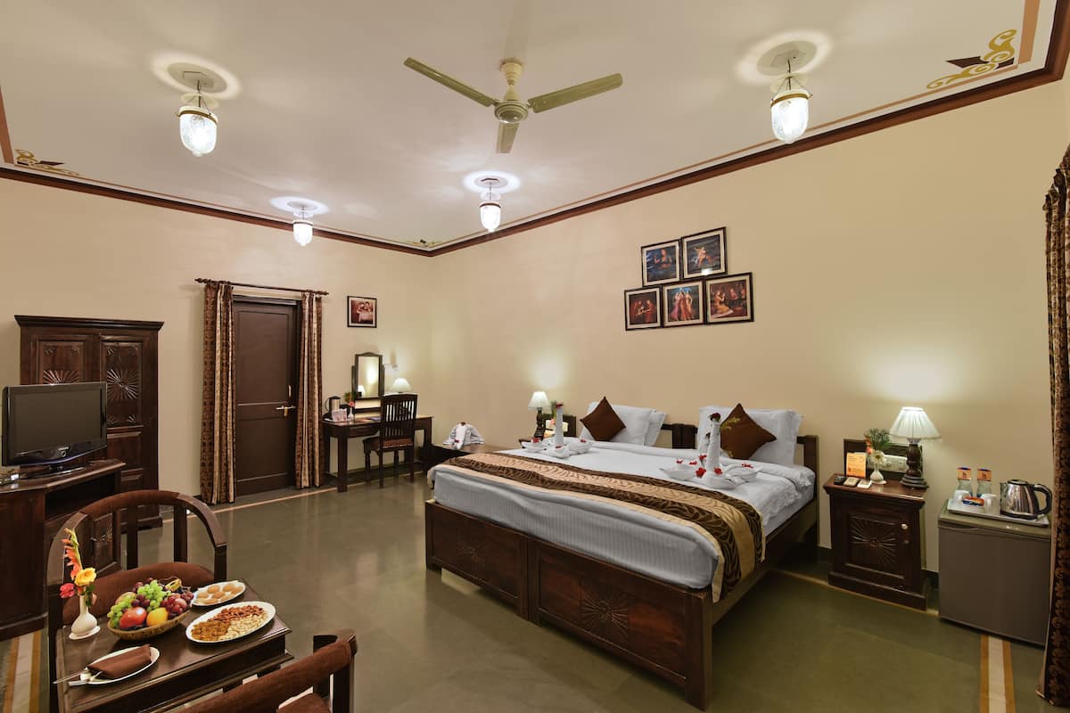 A hotel room with a large bed, a desk with a television, and a dining table with plates of food.