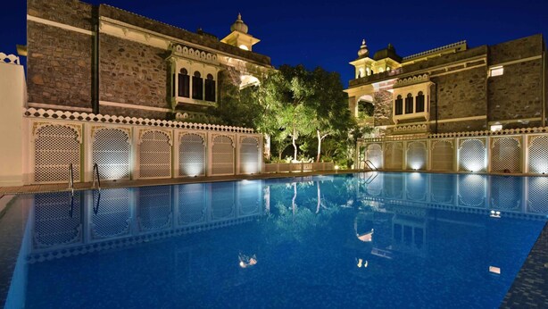 A swimming pool with a traditional architectural backdrop, surrounded by ornate lattice work and a night sky. - The Udai Bagh (Mavli)