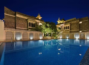 A swimming pool with a traditional architectural backdrop, surrounded by ornate lattice work and a night sky. - The Udai Bagh (Mavli)