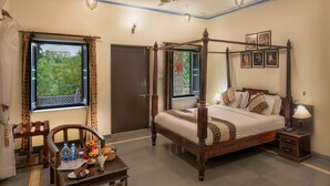 A four-poster bed with a wooden frame, a bedside table with a lamp, and a window with curtains. - The Udai Bagh (Mavli)