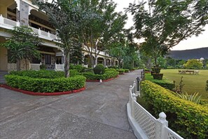A pathway flanked by lush greenery and a building with balconies. - The Udai Bagh (Mavli)