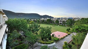A large, landscaped courtyard with a central lawn, surrounded by manicured gardens and a body of water. - The Udai Bagh (Mavli)