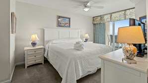 A hotel room with a bed, two bedside tables, a ceiling fan, a window with curtains, and a view of buildings.