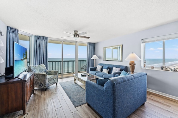 A living room with a sofa, a TV, a ceiling fan, and a view of the ocean. - Large 4 Bedroom Oceanfront Condo in North Myrtle Beach! | Ashworth - 1601 (North Myrtle Beach)