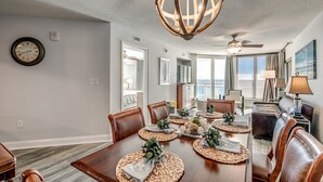 Un coin repas avec une table en bois dressée pour quatre personnes, entourée de fauteuils en cuir. Un grand et somptueux lustre est suspendu au-dessus de la table.