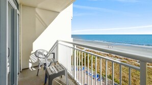 Ein Balkon mit Blick auf den Strand, ein Stuhl und ein Tisch.
